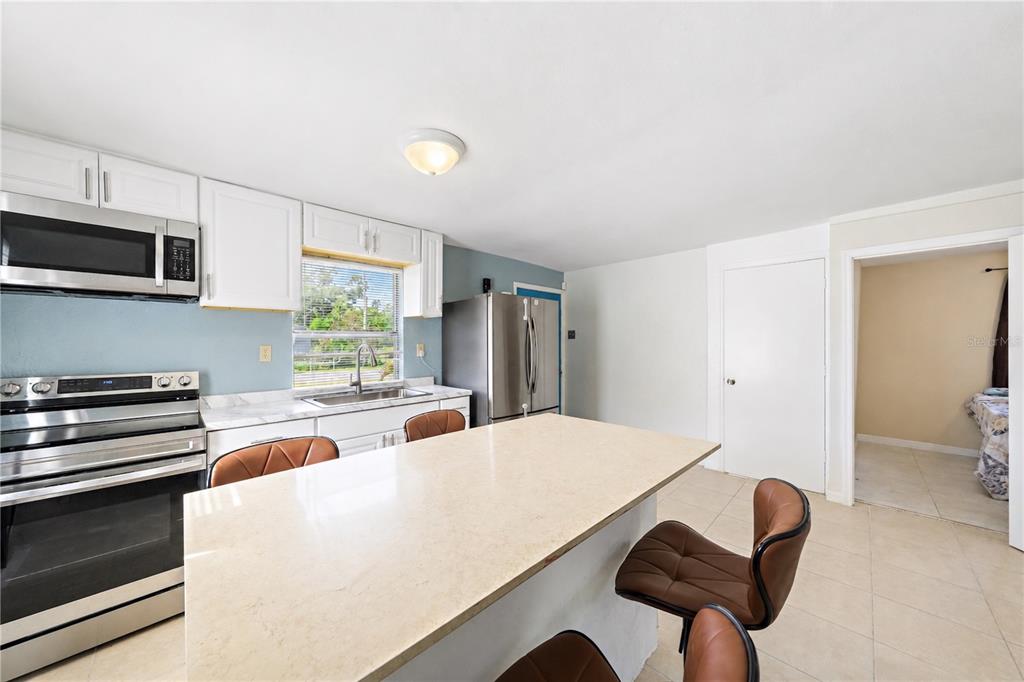 A kitchen features white cabinets, stainless steel appliances, a central island, and brown leather chairs — 516 29TH STREET E, PALMETTO, FL
