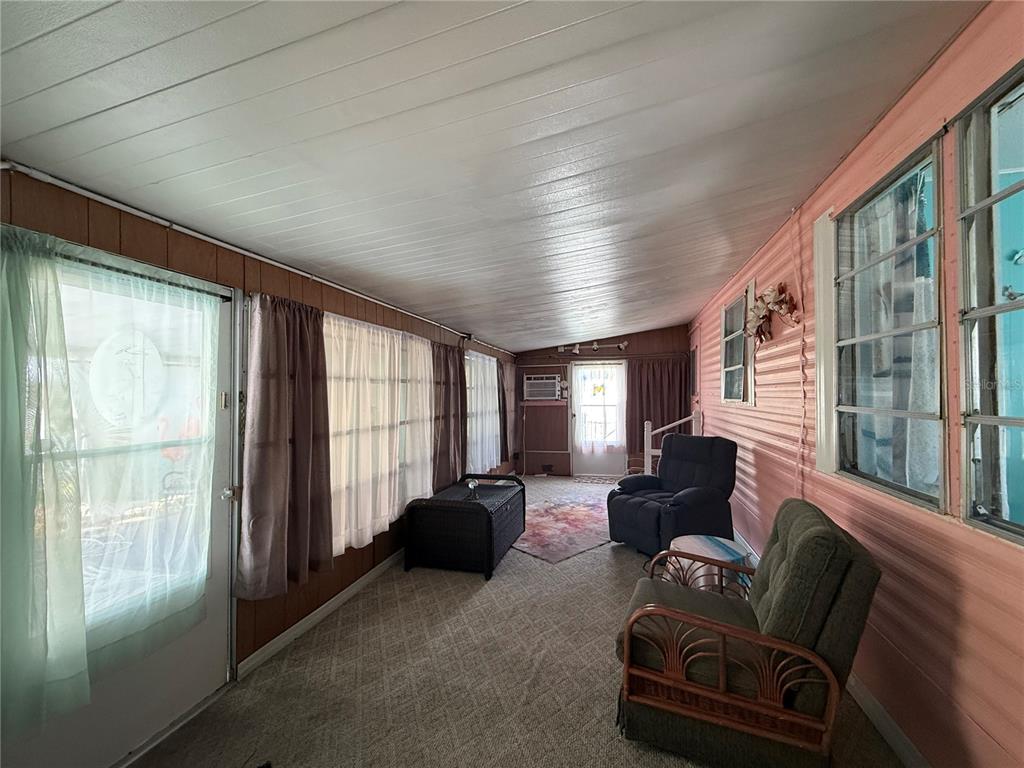 A sunroom features wood-paneled walls, a white ceiling, carpeted flooring, and several windows with curtains — 7703 AUDRY LANE, ELLENTON, FL