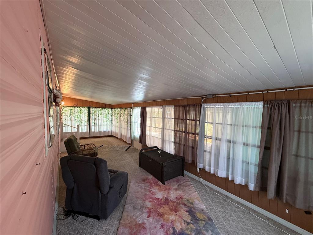 A sunroom features wood-paneled walls, a white sloped ceiling, carpeted flooring, and several armchairs — 7703 AUDRY LANE, ELLENTON, FL