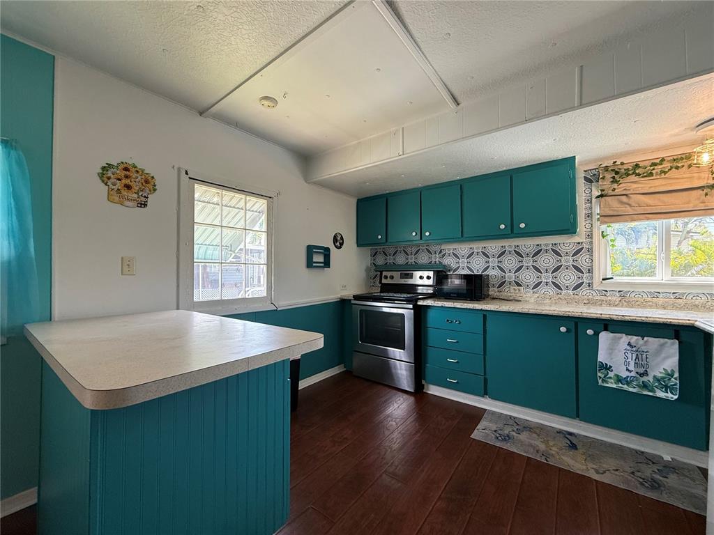 A kitchen features teal cabinets, patterned backsplash, stainless steel appliances, and a central island — 7703 AUDRY LANE, ELLENTON, FL