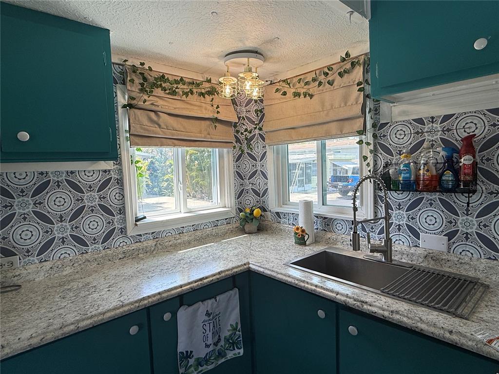 A kitchen features teal cabinets, patterned tile backsplash, granite countertops, and a stainless steel sink — 7703 AUDRY LANE, ELLENTON, FL