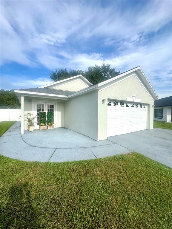 A light-colored house exterior features a two-car garage, a concrete driveway, and a side entrance — 2412 SONJA COURT, KISSIMMEE, FL