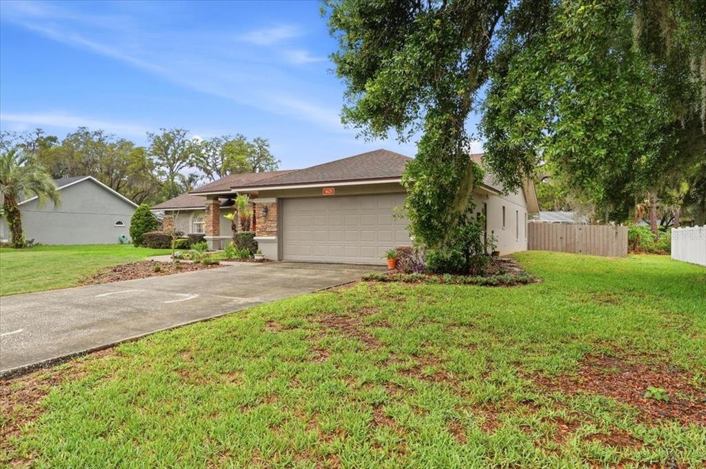 A single-story house with a beige garage and a concrete driveway under a large tree — 1620 YEOMANS PATH, LAKELAND, FL