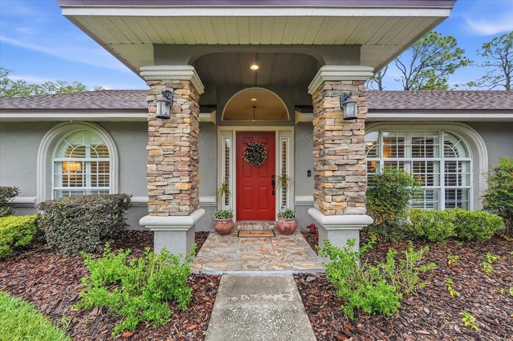 The exterior of a house features a red front door between two stone-clad columns — 1620 YEOMANS PATH, LAKELAND, FL