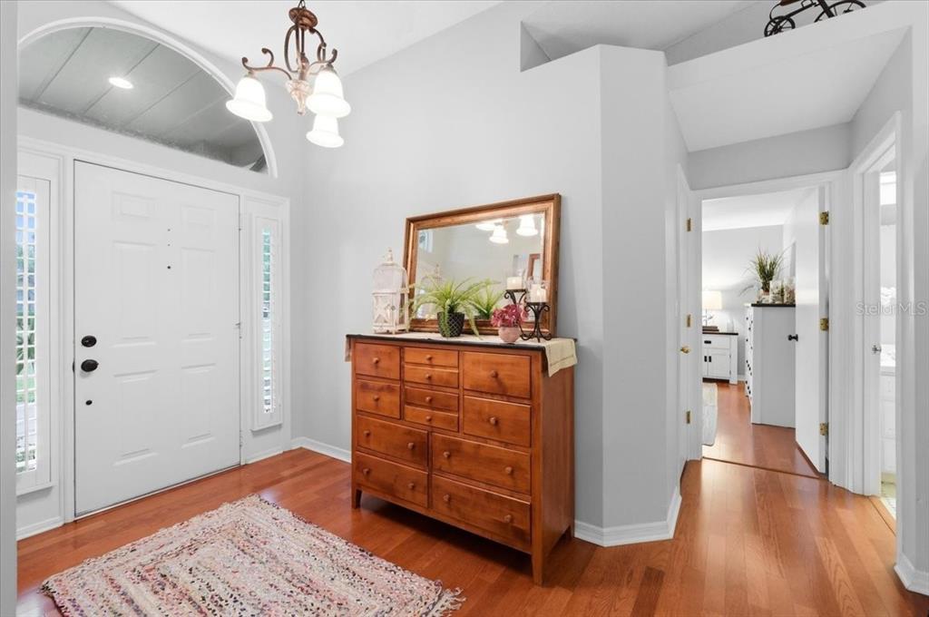 An entryway features a wooden dresser, a mirror, a chandelier, and hardwood flooring — 1620 YEOMANS PATH, LAKELAND, FL