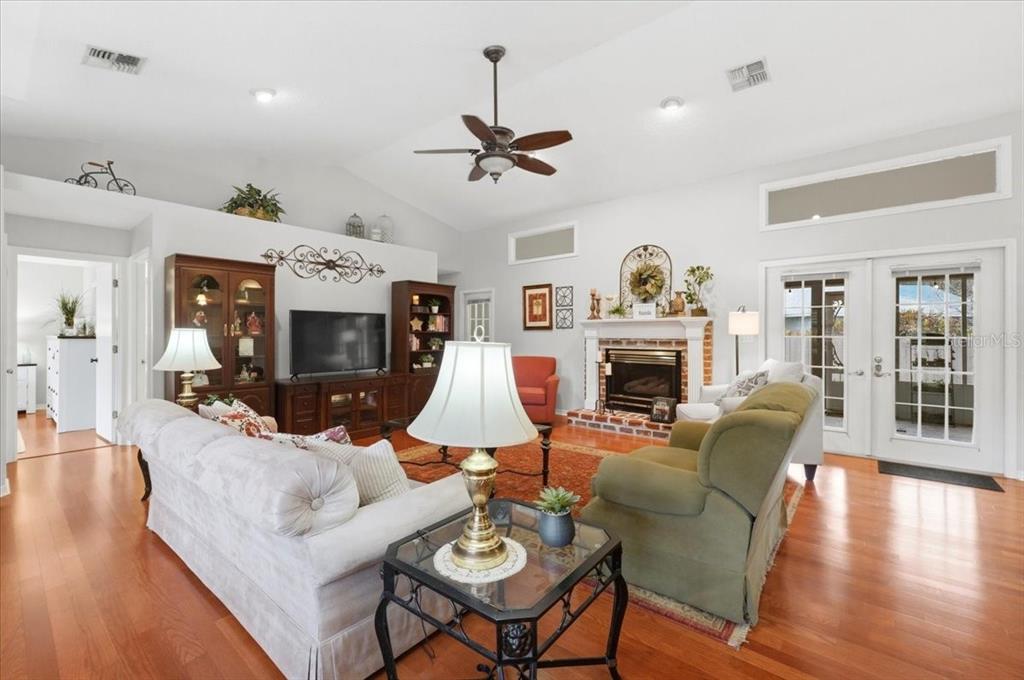 A living room features hardwood floors, a brick fireplace, and a vaulted ceiling with a fan — 1620 YEOMANS PATH, LAKELAND, FL