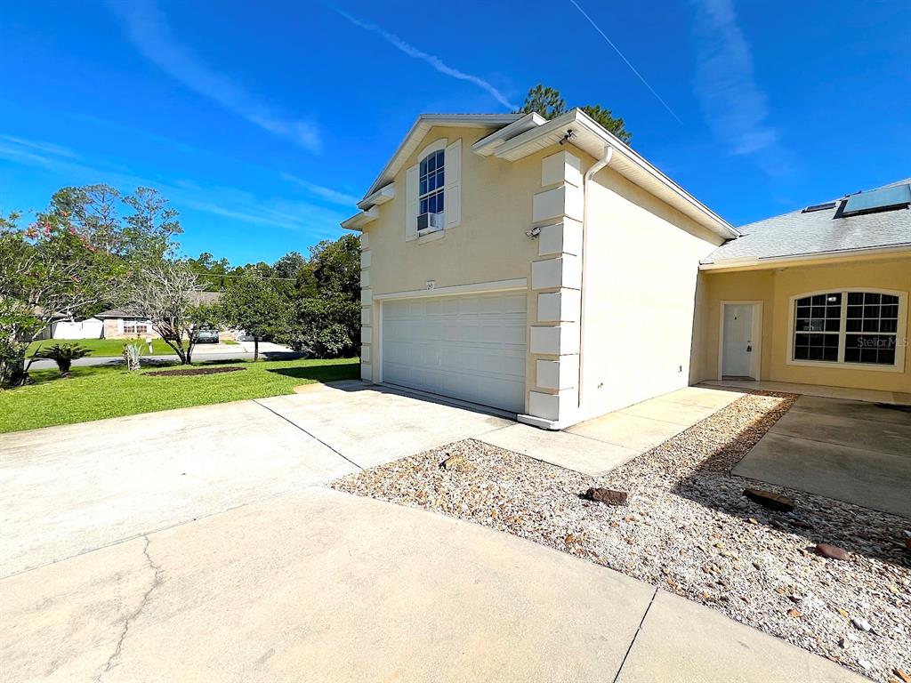 A beige house exterior features a two-car garage, a white front door, and a driveway — 20 REGIS LANE UNIT A, PALM COAST, FL