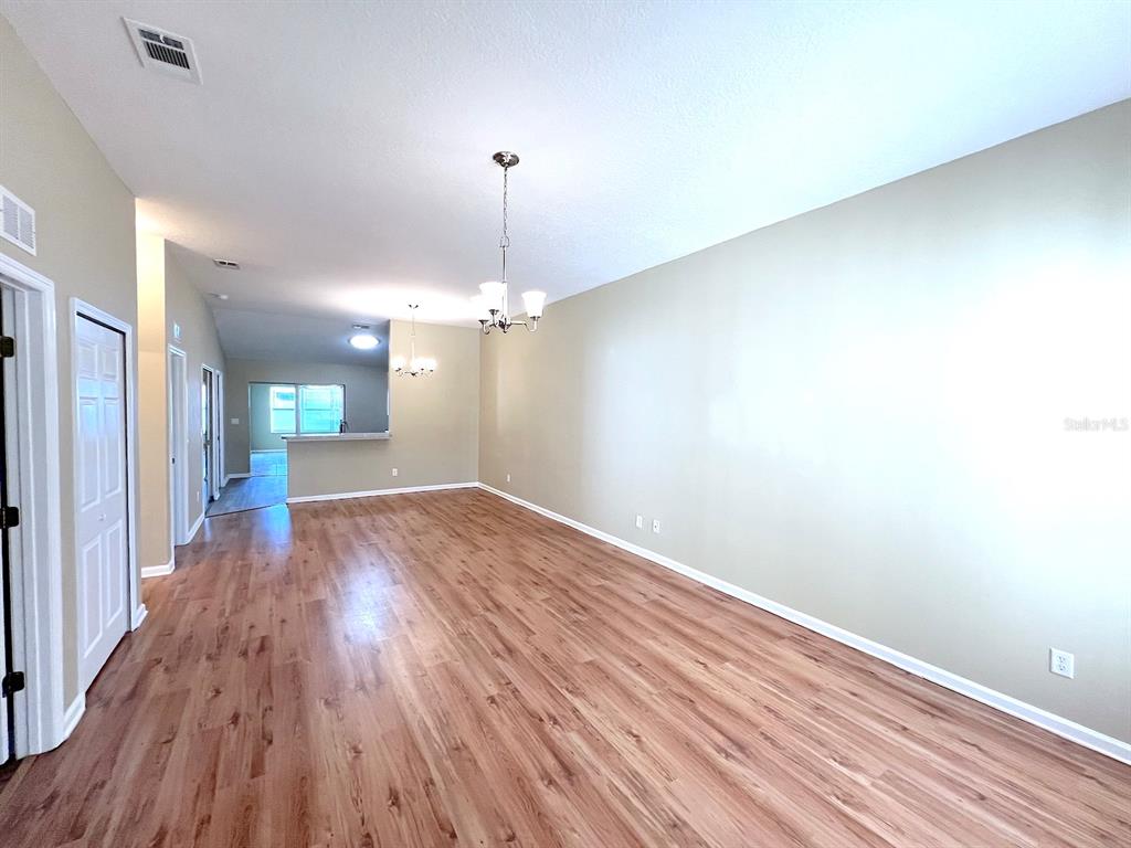 A spacious living area features light wood-look flooring, beige walls, and two hanging light fixtures — 20 REGIS LANE UNIT A, PALM COAST, FL