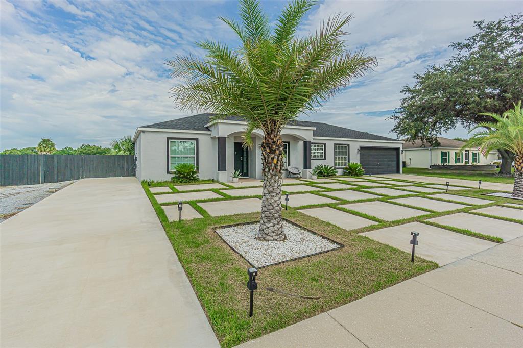 A single-story house with a gray exterior, dark garage door, and a grid-patterned concrete driveway — 12121 COLONIAL ESTATES LANE, RIVERVIEW, FL