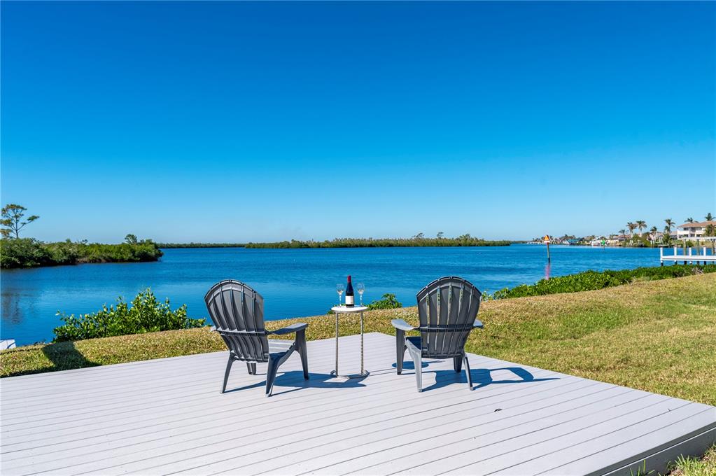 Two gray Adirondack chairs and a small table sit on a deck overlooking water — 5117 COLLINGSWOOD BOULEVARD, PORT CHARLOTTE, FL