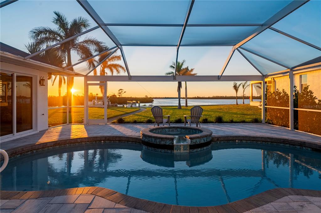 A screened-in pool and hot tub overlook a grassy lawn and a sunset water view — 5117 COLLINGSWOOD BOULEVARD, PORT CHARLOTTE, FL