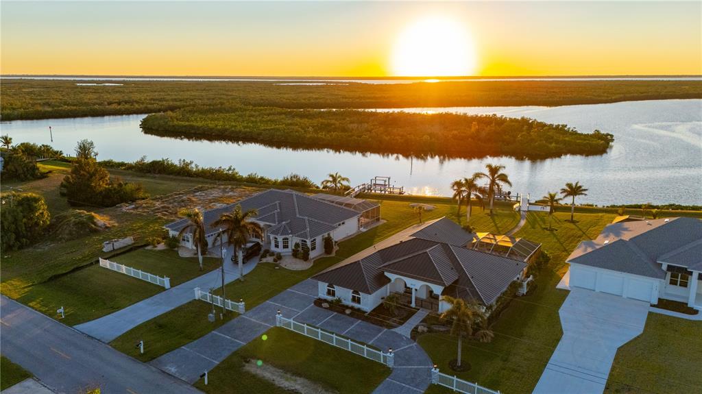 An aerial view of waterfront houses with palm trees and a sunset over the water — 5117 COLLINGSWOOD BOULEVARD, PORT CHARLOTTE, FL