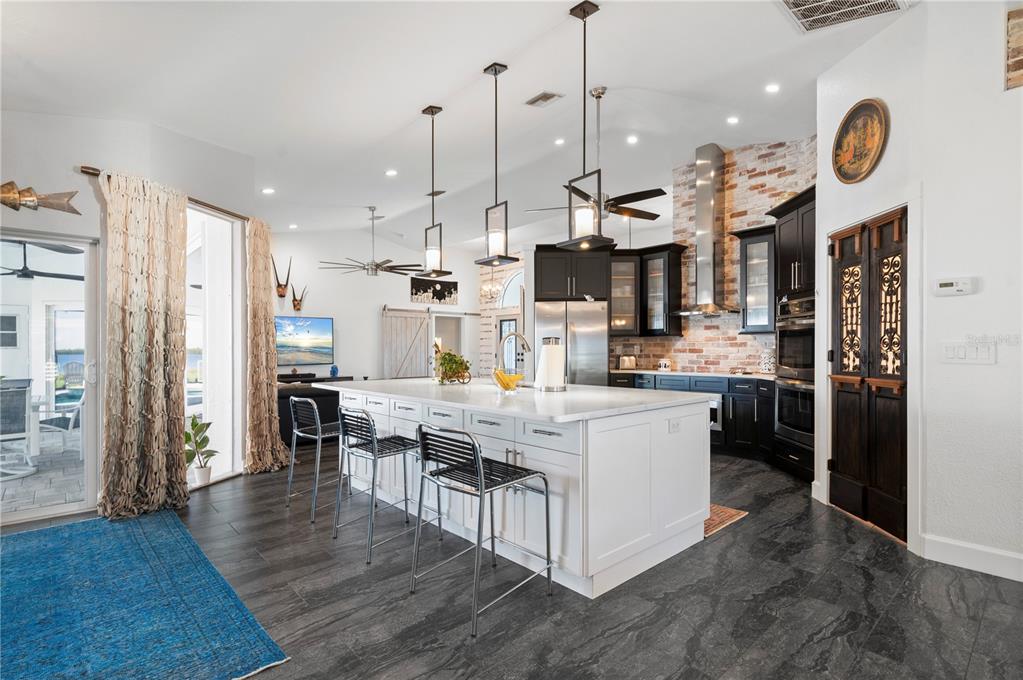 A modern kitchen features a large white island, dark cabinetry, and a brick backsplash — 5117 COLLINGSWOOD BOULEVARD, PORT CHARLOTTE, FL