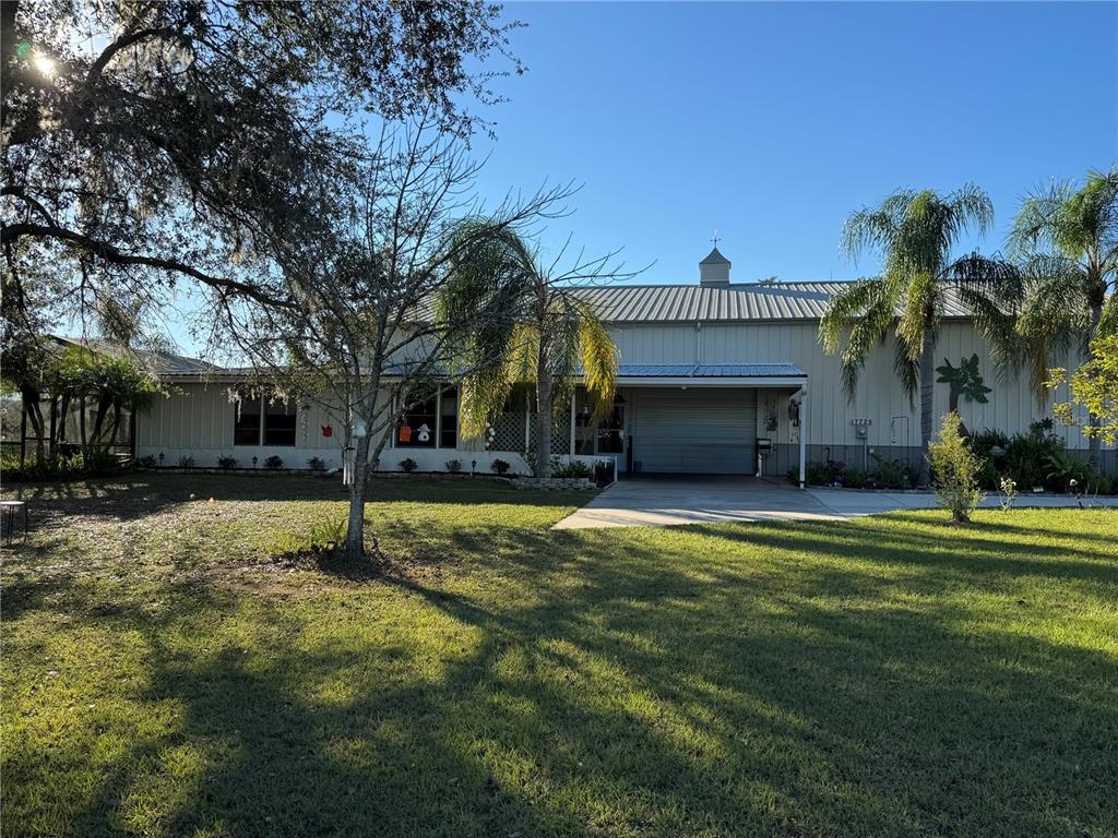 A metal-sided house with a metal roof, a garage bay, and palm trees in front — 17725 POWERLINE ROAD, DADE CITY, FL
