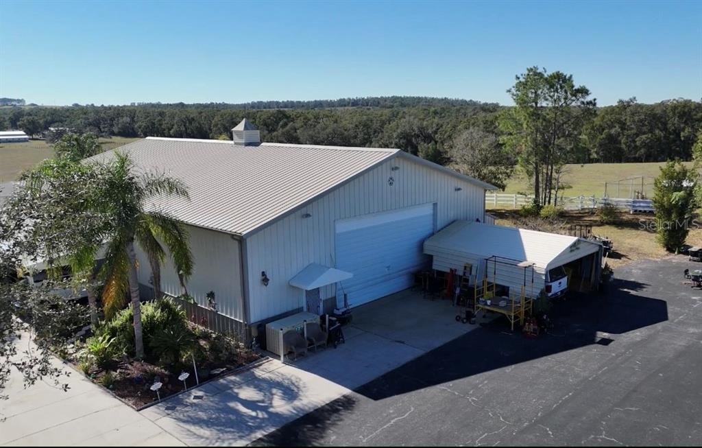 An aerial view shows a large metal workshop building with a carport and surrounding landscape — 17725 POWERLINE ROAD, DADE CITY, FL