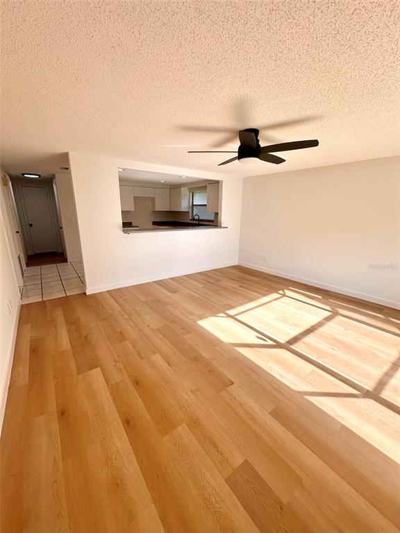 A living room with light wood-look flooring, a ceiling fan, and a kitchen pass-through window — 15717 AVALON AVENUE, CLEARWATER, FL