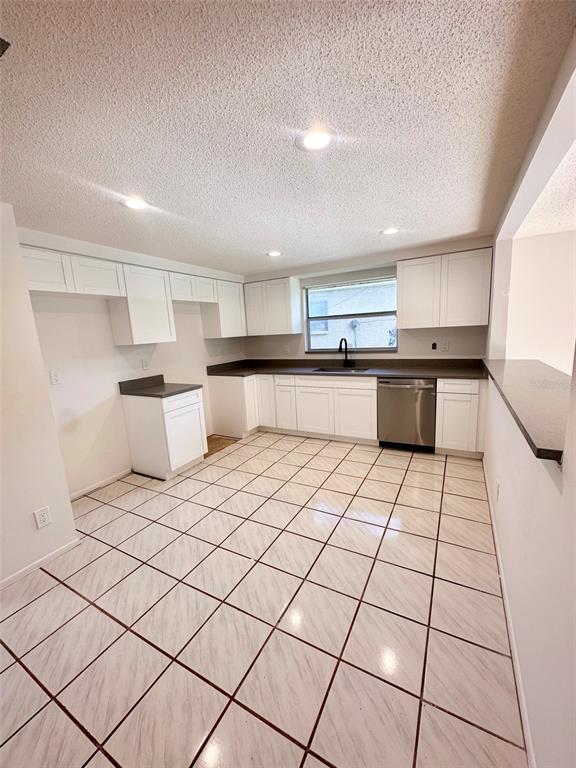 A kitchen features white cabinets, dark countertops, tile flooring, and a stainless steel dishwasher — 15717 AVALON AVENUE, CLEARWATER, FL