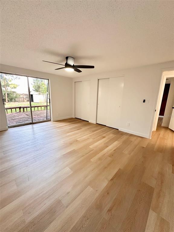 A bedroom with light wood-look flooring, a ceiling fan, and sliding glass doors to a deck — 15717 AVALON AVENUE, CLEARWATER, FL