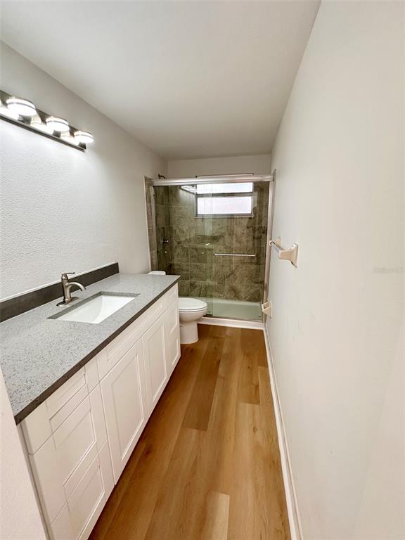 A bathroom features a white vanity with a gray countertop, wood-look flooring, and a glass-enclosed shower — 15717 AVALON AVENUE, CLEARWATER, FL