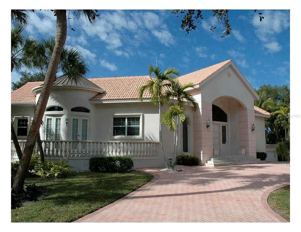 A single-story house with a light-colored stucco exterior, a tiled roof, and a brick driveway — 5331 SIESTA COVE DRIVE, SARASOTA, FL