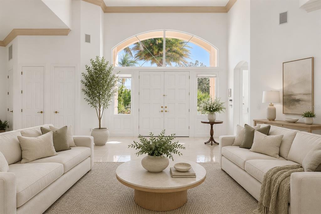 A bright living room features two white sofas, a round coffee table, and double entry doors — 5331 SIESTA COVE DRIVE, SARASOTA, FL
