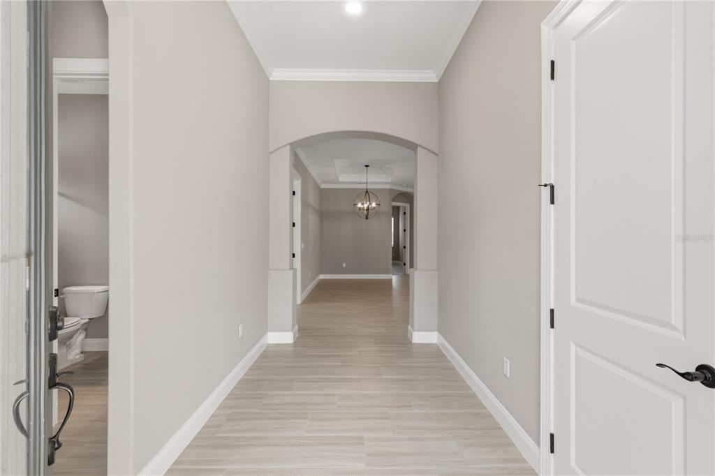 A bright entryway features light-colored wood-look tile flooring, gray walls, and an arched hallway opening — 7 OASIS CIRCLE, PALM COAST, FL