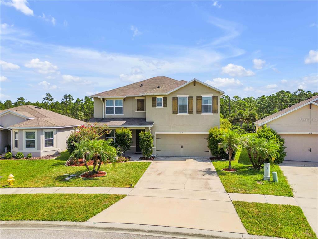 A two-story suburban house with a beige stucco exterior, a two-car garage, and landscaping — 5215 BEAR CORN RUN, PORT ORANGE, FL