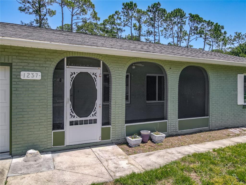A covered porch features green painted brick arches, a ceiling fan, and a concrete floor — 1237 JEFFERY DRIVE, PORT ORANGE, FL