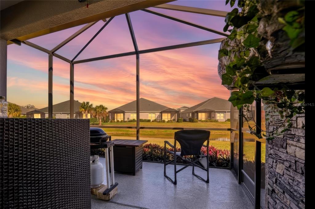 A screened-in patio overlooks a pond and neighboring houses during a sunset — 14530 BAREFOOT LANE, PARRISH, FL