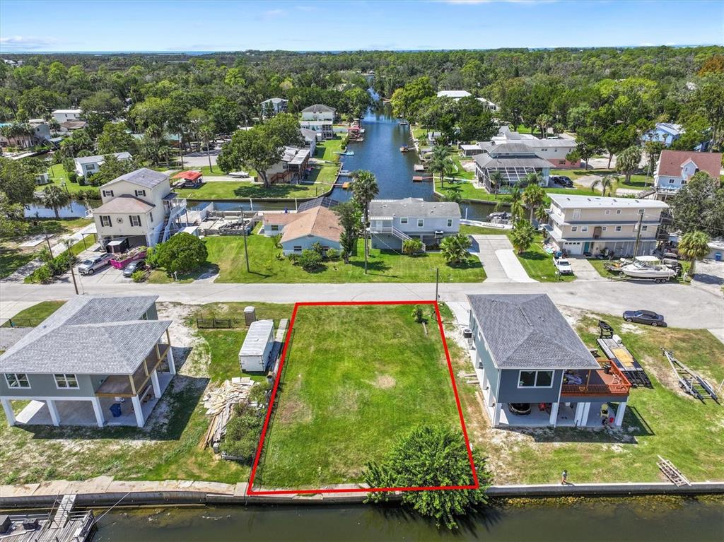 An aerial view shows a vacant waterfront lot outlined in red between two elevated houses — 6262 ISLAND DRIVE, SPRING HILL, FL