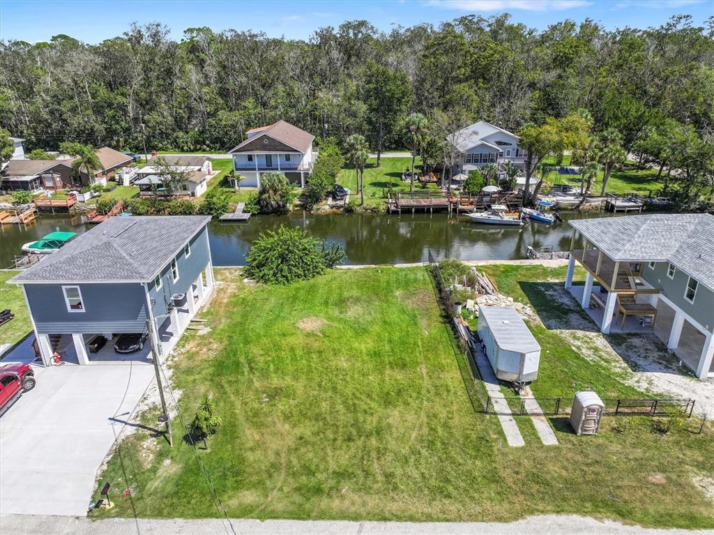 An aerial view shows a vacant grassy lot situated between two elevated houses near water — 6262 ISLAND DRIVE, SPRING HILL, FL
