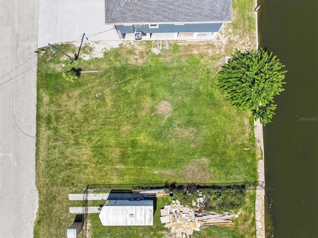 An aerial view shows a grassy residential lot bordering a canal with a small shed — 6262 ISLAND DRIVE, SPRING HILL, FL