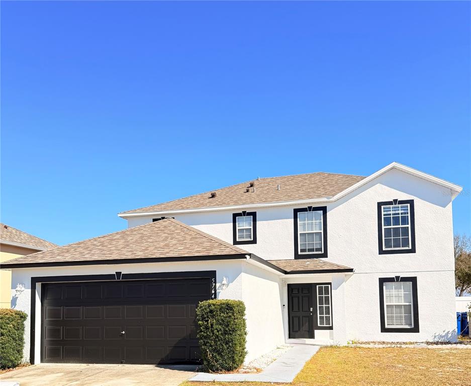 A two-story house with white stucco walls, a dark garage door, and a shingled roof — 5764 ROYAL HILLS CIRCLE, WINTER HAVEN, FL