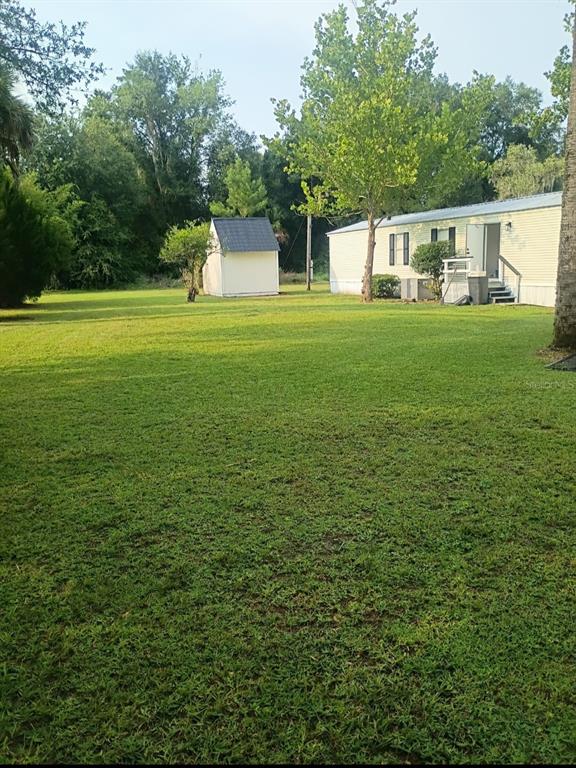 A grassy backyard features a small storage shed and a light-colored mobile home — 105 CANARY LANE, SATSUMA, FL