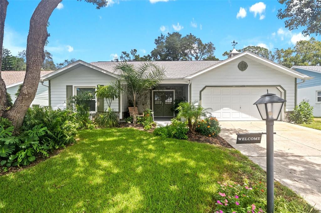 A single-story house with light siding, a two-car garage, and a landscaped front yard — 6342 PINE MEADOWS DRIVE, SPRING HILL, FL