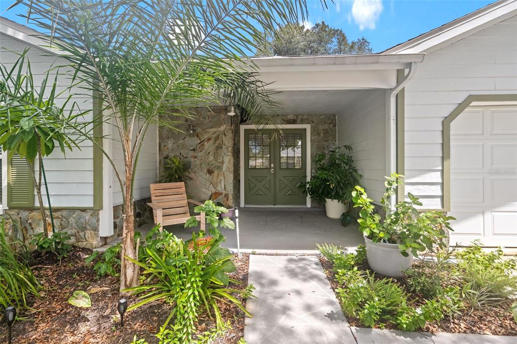 A covered front porch features a stone wall, green double doors, and potted plants — 6342 PINE MEADOWS DRIVE, SPRING HILL, FL