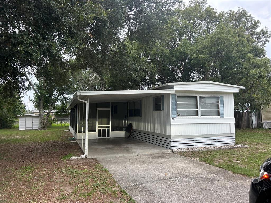 A white mobile home with a carport, basketball hoop, and surrounding trees on a grassy lot — 9640 SE 161ST PLACE, SUMMERFIELD, FL