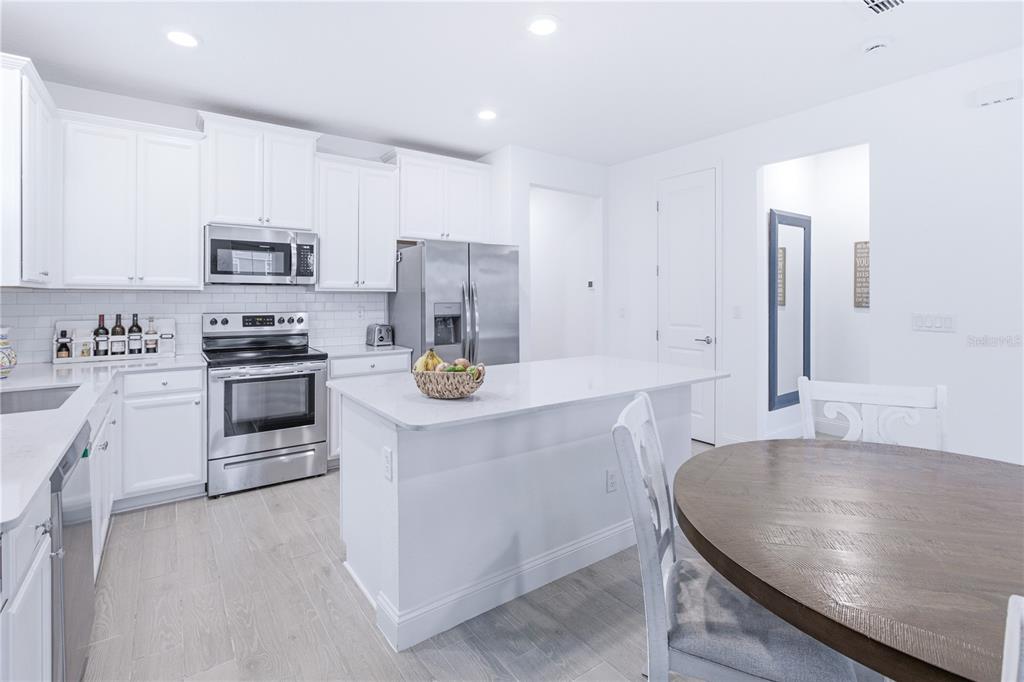 A modern kitchen features white cabinetry, stainless steel appliances, a center island, and wood-look flooring — 43 TYSON COURT, ST AUGUSTINE, FL