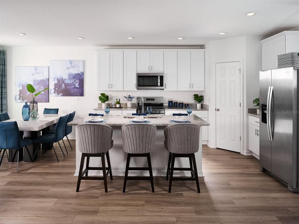 A modern kitchen features white cabinets, a granite island with three stools, and stainless appliances — 833 SILVERADO TRAIL DRIVE, LAKE HAMILTON, FL