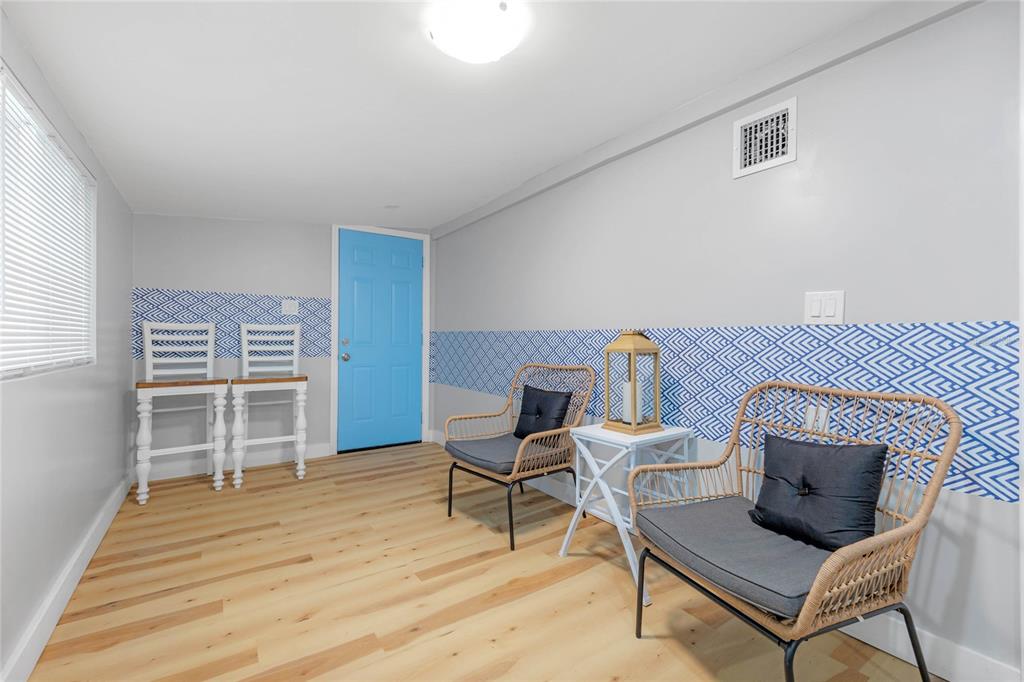 A room with light wood floors, blue patterned wall accents, two wicker chairs, and a door — 4809 THORPE AVENUE, ORLANDO, FL