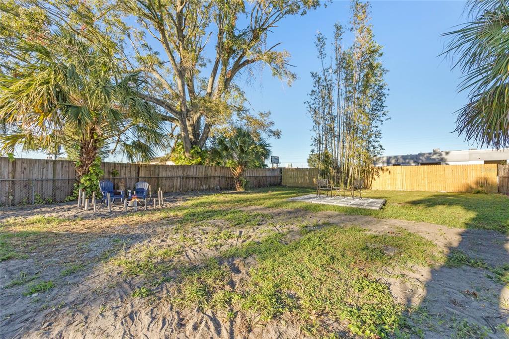 A backyard features a sandy lawn, a small patio, two seating areas, and tall trees — 4809 THORPE AVENUE, ORLANDO, FL