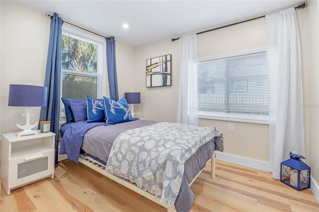 A bedroom with light wood flooring, a bed with blue bedding, and two windows — 4809 THORPE AVENUE, ORLANDO, FL