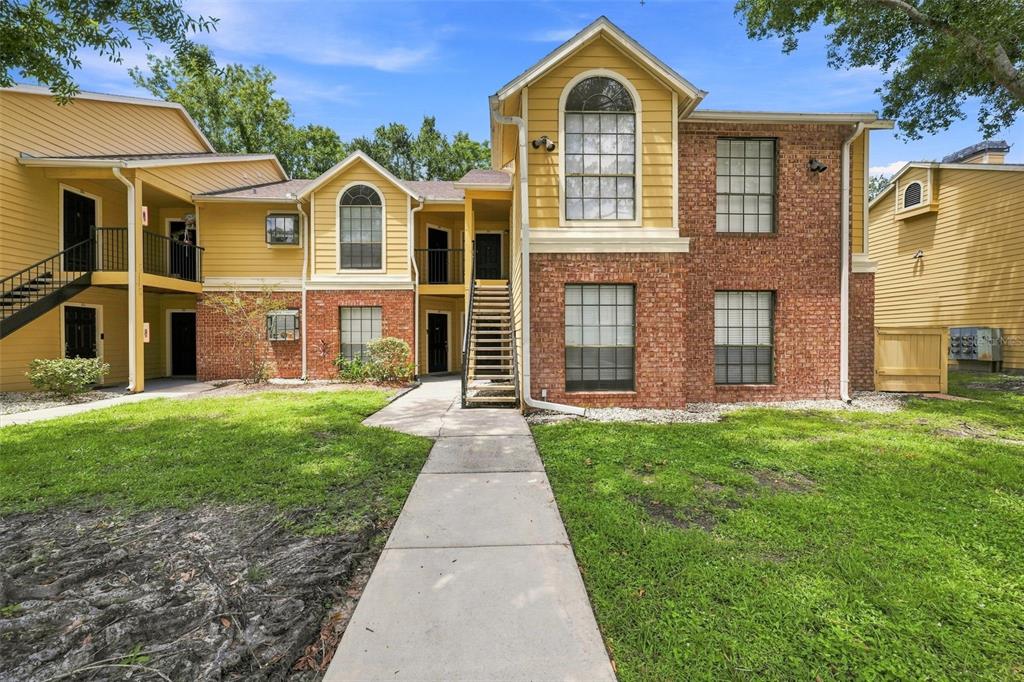 A two-story apartment building with yellow siding, brick accents, and an outdoor staircase — 8630 MALLARD RESERVE DRIVE UNIT 203, TAMPA, FL