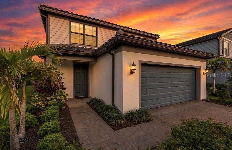 A two-story house with a gray garage, a paved walkway, and a palm tree at sunset — 6111 BLUESTAR COURT, LAKEWOOD RANCH, FL