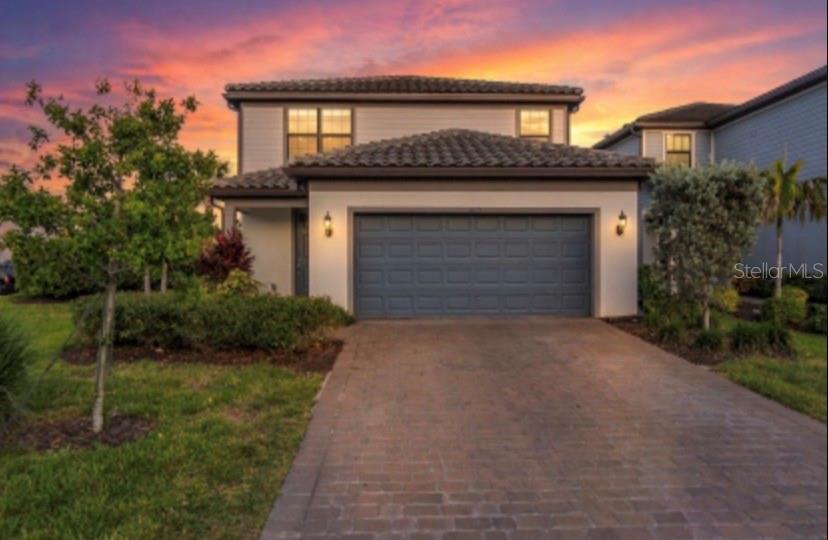 A two-story house with a tiled roof, a gray garage door, and a brick driveway — 6111 BLUESTAR COURT, LAKEWOOD RANCH, FL