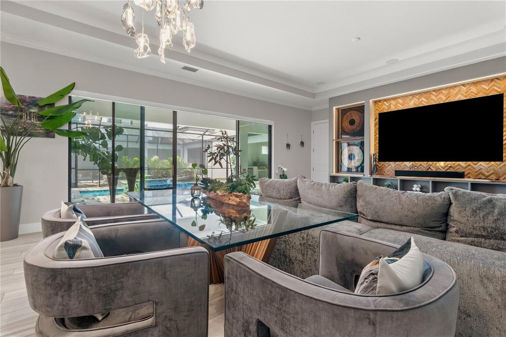A modern living room features a glass dining table, velvet chairs, and a large television — 10782 TORCHWOOD SEA WAY, SAN ANTONIO, FL