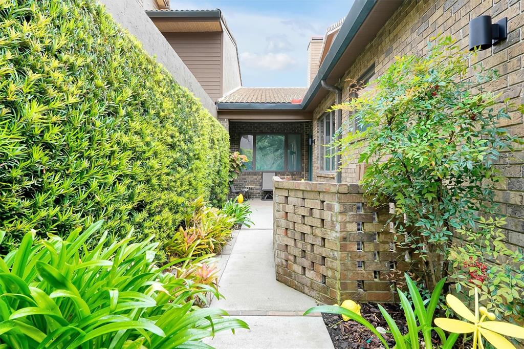 A concrete walkway leads between a tall hedge and a brick wall toward a house — 139 WODEN WAY, WINTER HAVEN, FL