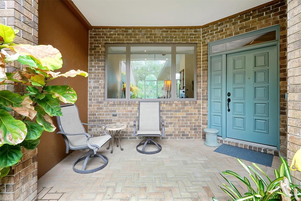 A covered brick patio features a teal front door, two chairs, and a large window — 139 WODEN WAY, WINTER HAVEN, FL