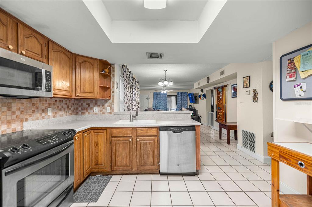 A kitchen with wood cabinets, stainless steel appliances, and tile flooring opens to a living area — 964 5TH STREET UNIT 964, CLERMONT, FL
