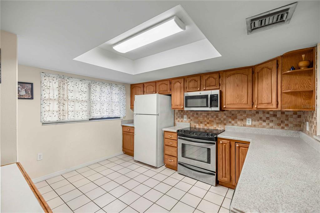 A kitchen with wood cabinets, stainless steel appliances, a white refrigerator, and tiled flooring — 964 5TH STREET UNIT 964, CLERMONT, FL